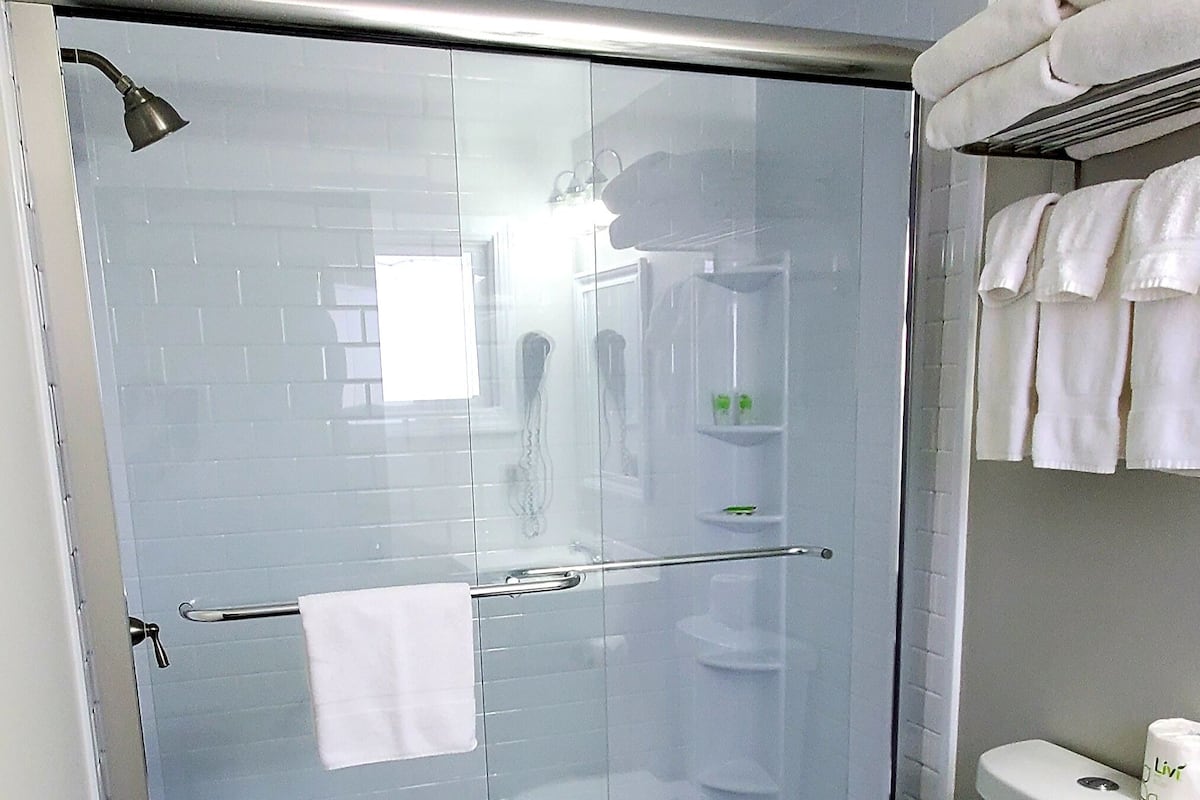 A modern bathroom with a glass-enclosed shower, a white toilet, and a towel rack with white towels.