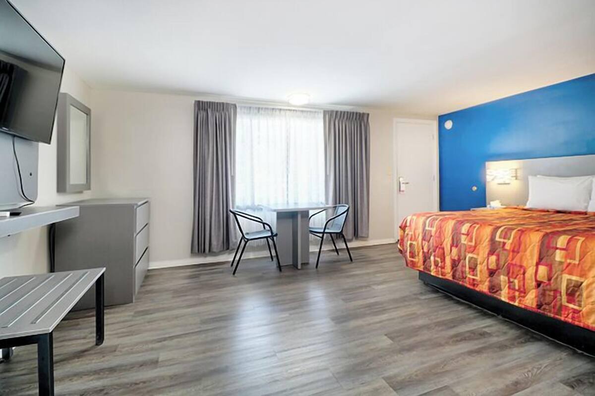 A hotel room with a bed, a desk with a chair, a television, and a window with curtains.