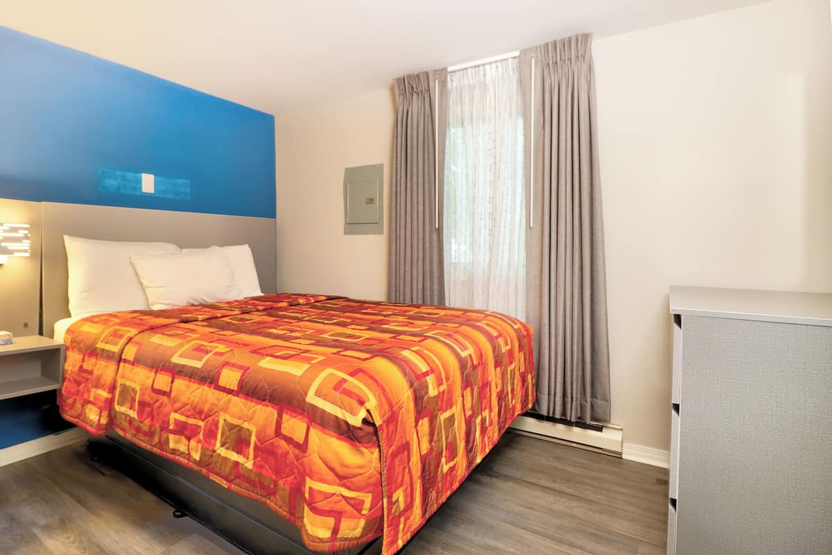 A hotel room with a bed, a nightstand, a desk, a chair, and a window with curtains.