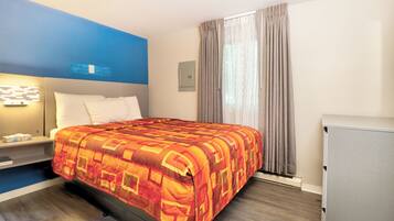 A hotel room with a bed, a nightstand, a desk, a chair, and a window with curtains.