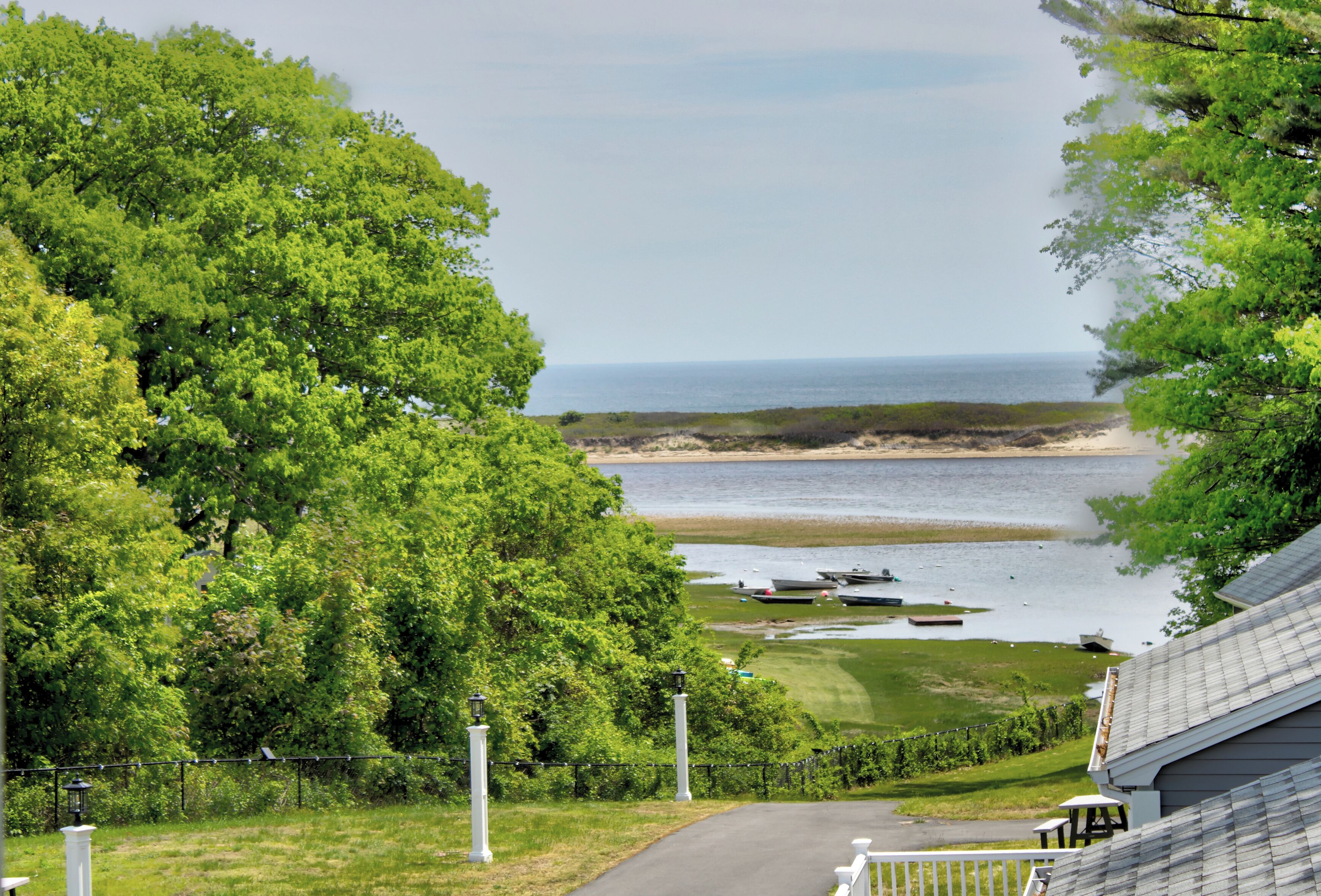 A coastal view with a pathway leading to a beach, boats, and lush greenery.