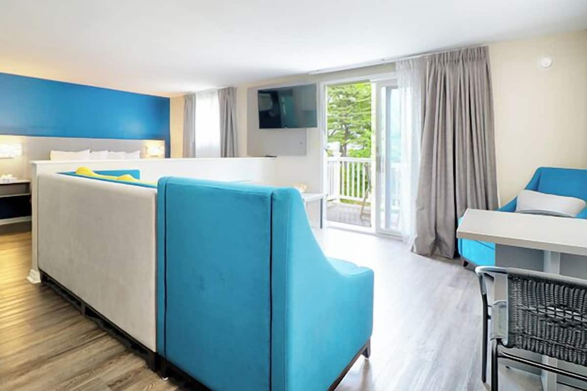 A hotel room with a bed, a desk, a chair, a TV, and a balcony with a view.