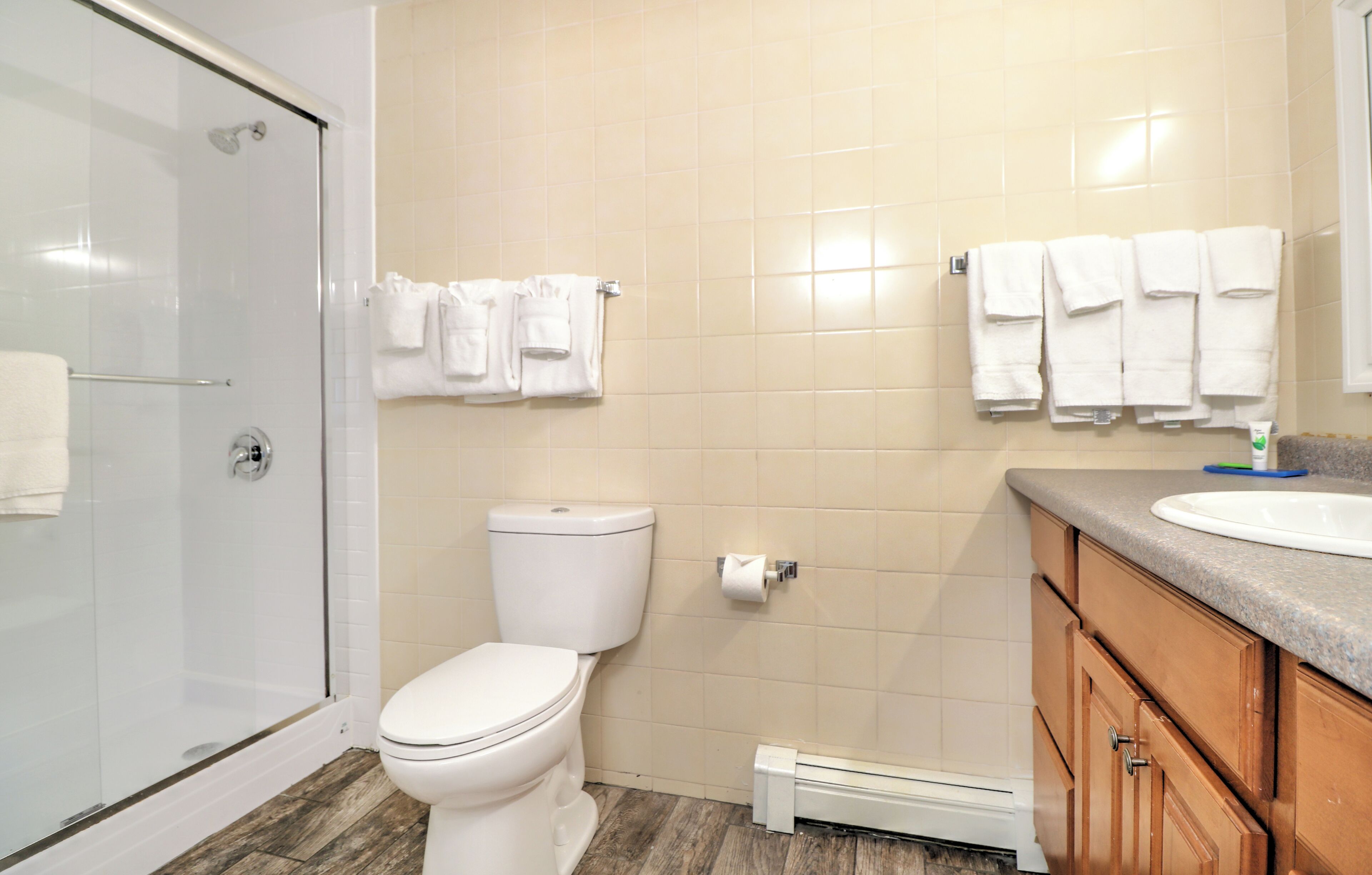 A bathroom with a glass shower enclosure, a toilet, a sink with a countertop, and wooden cabinets.