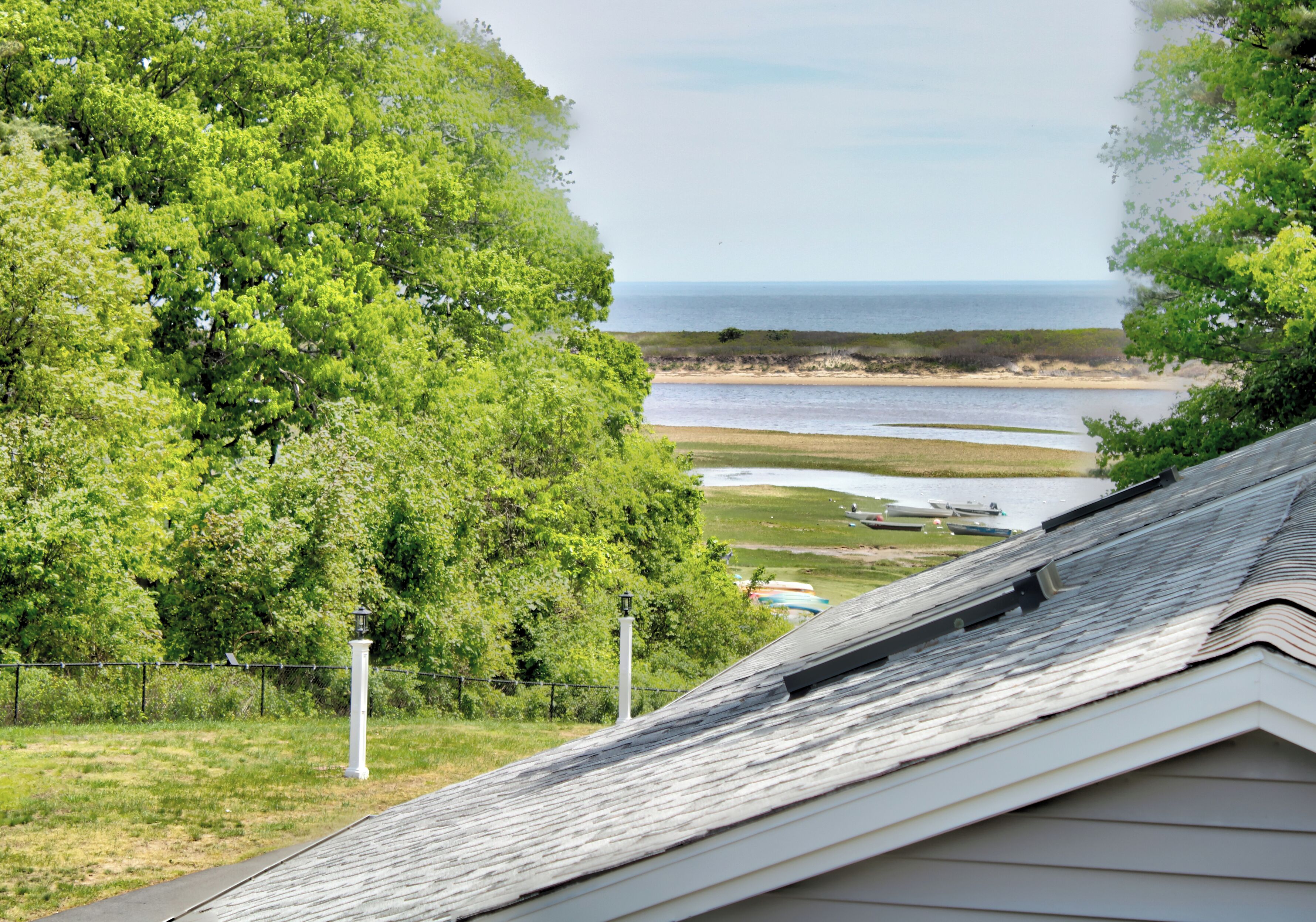 A coastal view with a grassy area, a white fence, and a lighthouse.