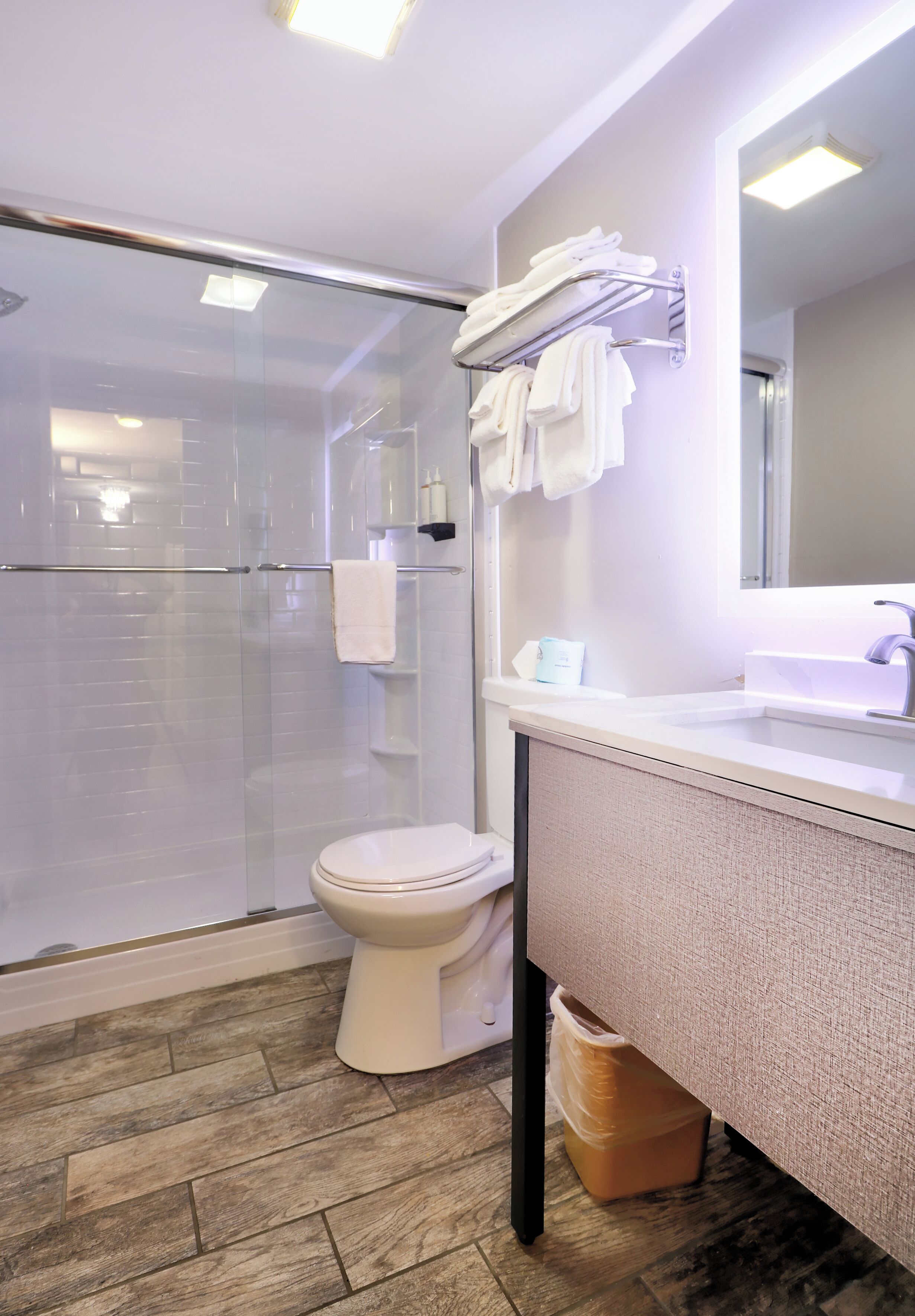 Een moderne badkamer met een douchecabine van glas, een toilet, een wastafel met spiegel en een handdoekrek.
