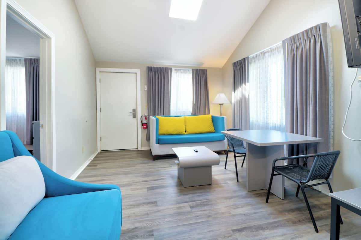 A modern hotel room with a sofa, a small table, a chair, and a desk.