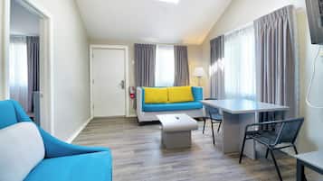 A modern hotel room with a sofa, a small table, a chair, and a desk.