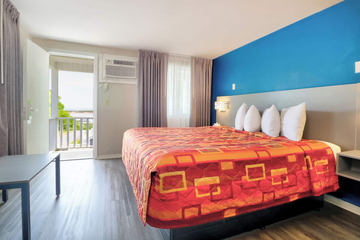 A hotel room with a bed, a desk, a balcony, and a view of the outdoors.