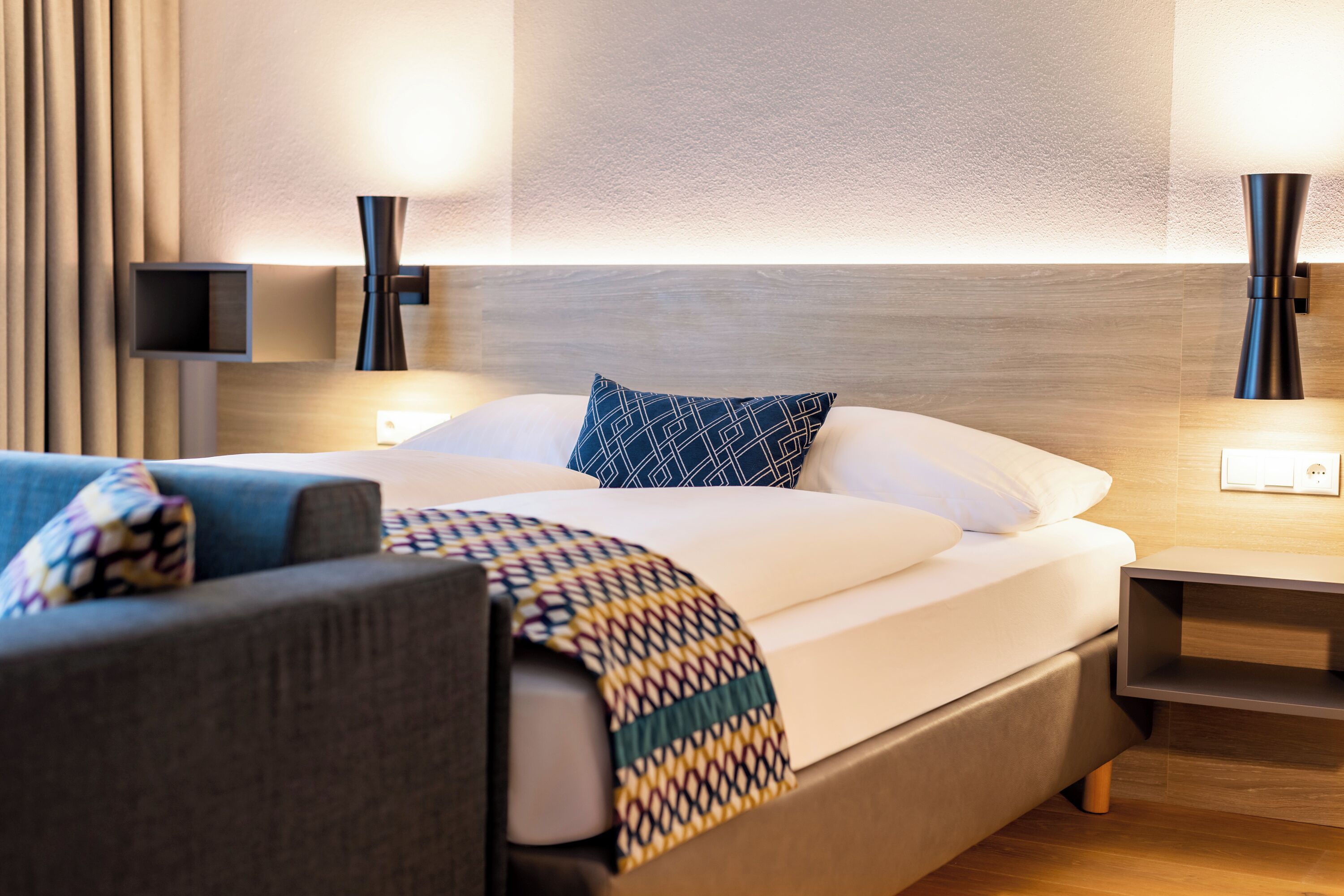 Een moderne hotelkamer met een net opgemaakt bed, een bank en een nachtkastje.