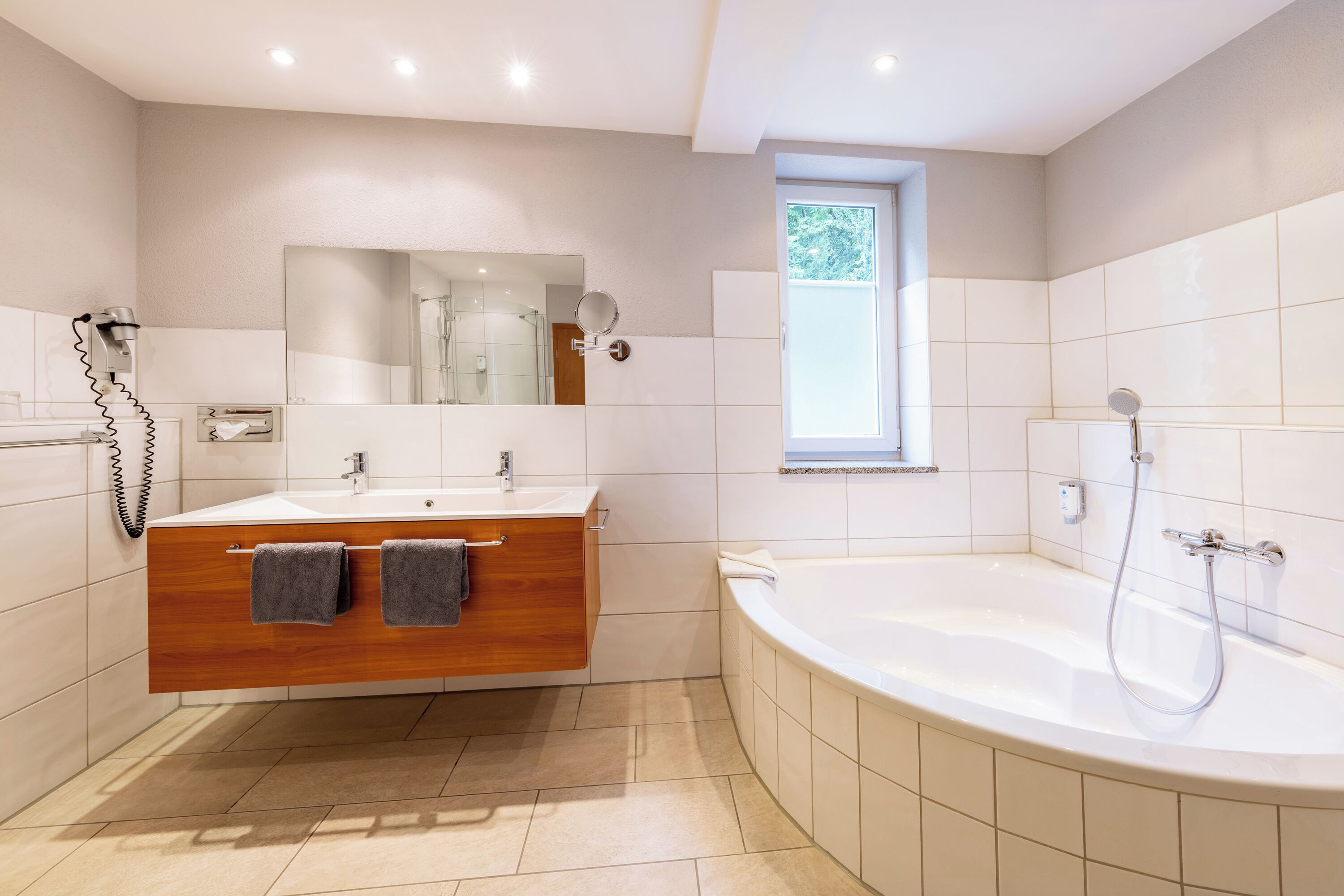 A modern bathroom with a wooden vanity, a large bathtub, and a mirror above the sink.