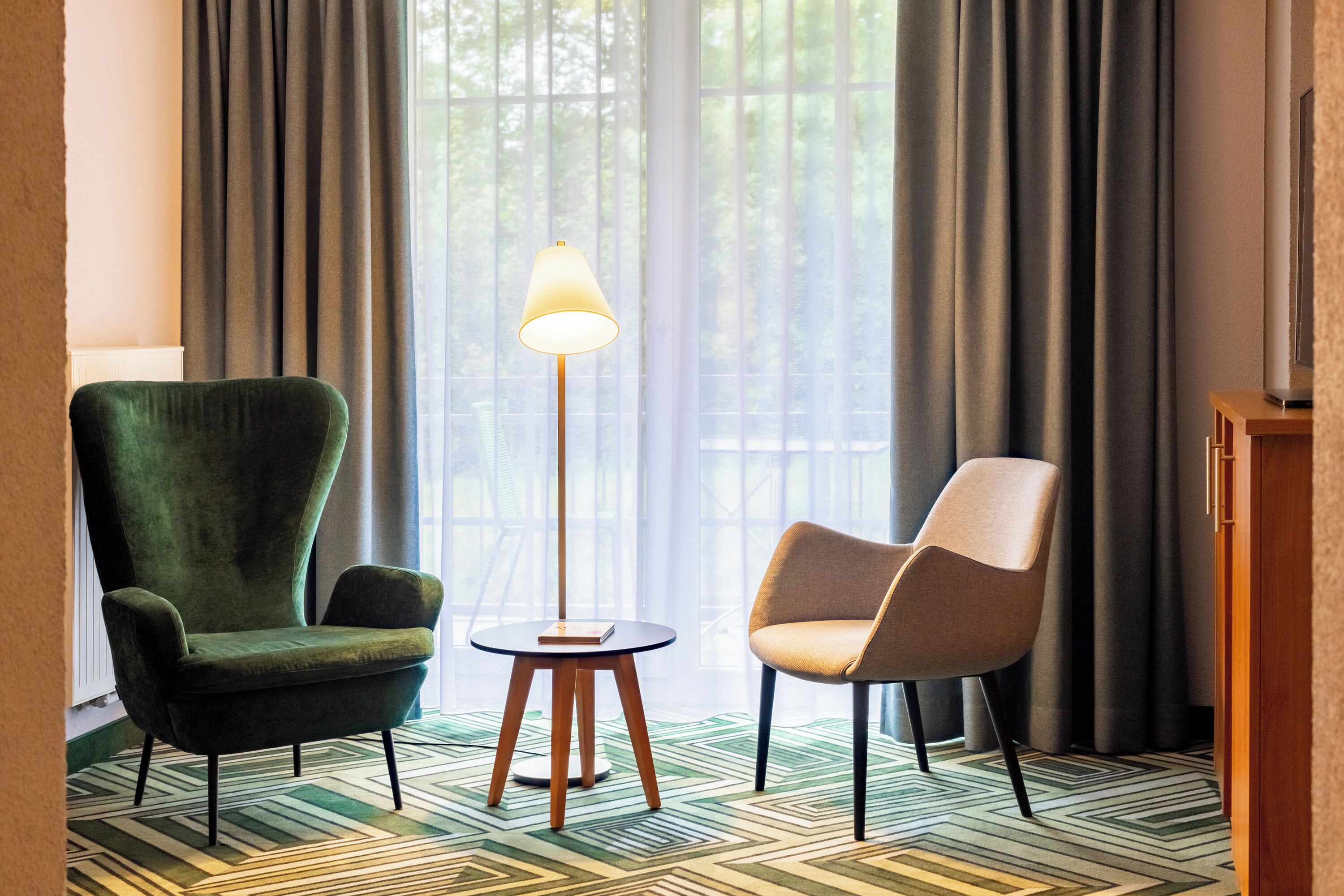 Una habitación con un sillón verde, un sillón color beige y una lámpara de pie.