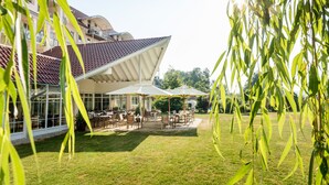 A building with a covered patio area, outdoor seating, and a view of the surrounding greenery. - Parkhotel Maximilian Ottobeuren Resort&Spa (Ottobeuren)