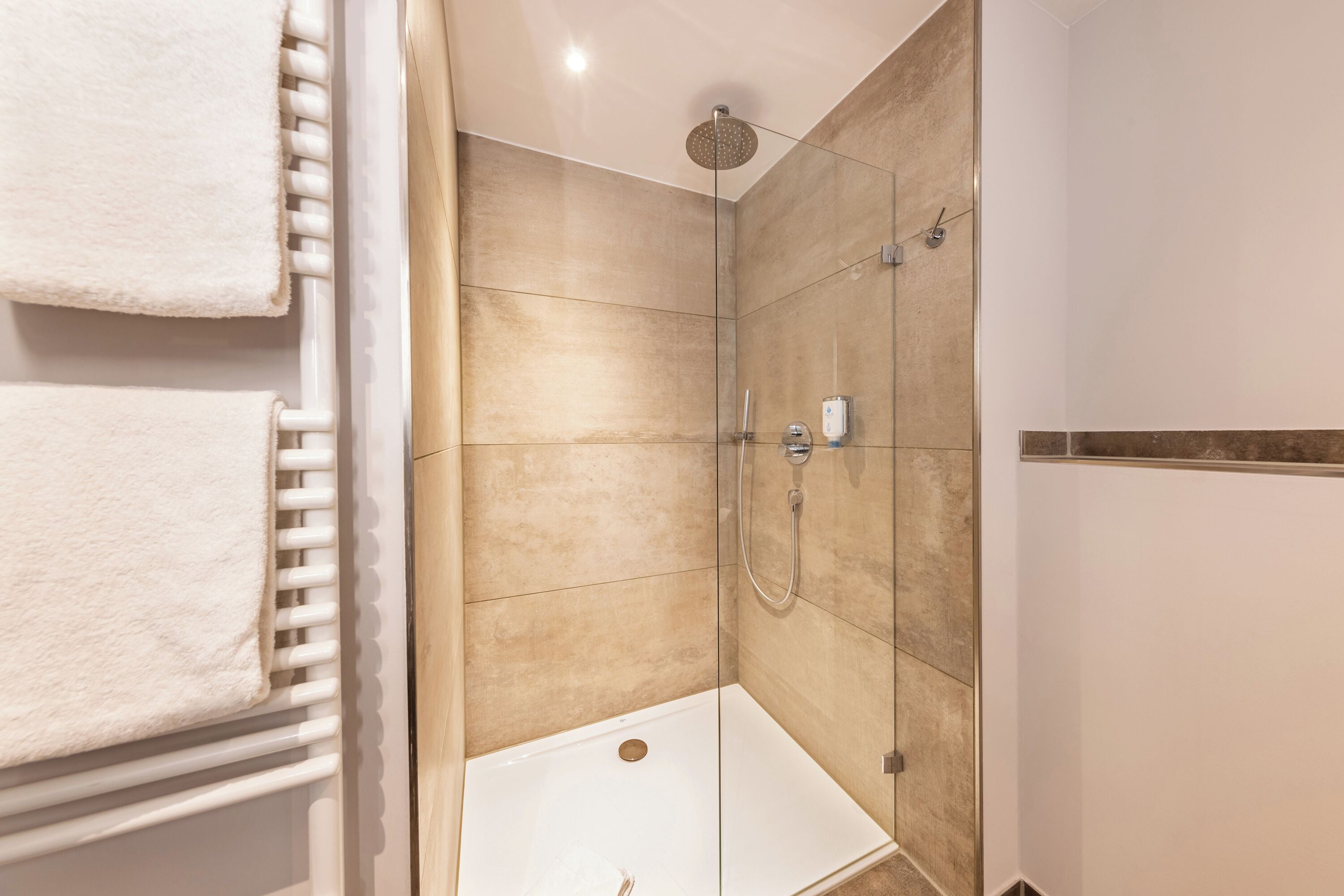 A modern bathroom with a glass shower enclosure, a white towel rack, and beige tiles.