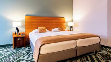 A hotel room with a large bed, two bedside lamps, a wooden headboard, and a patterned carpet.