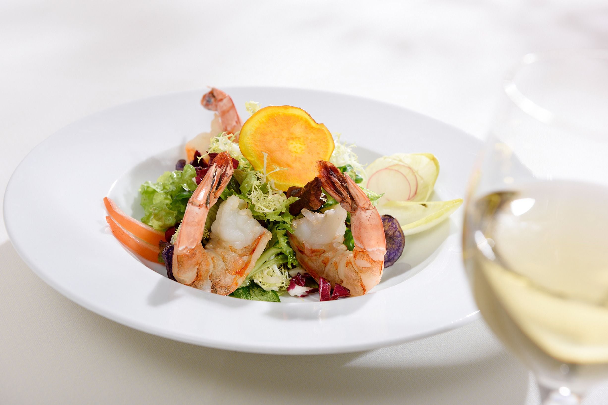 Uma salada de camarão com uma fatia de laranja e rabanete sobre um prato branco.