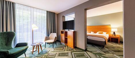 A hotel room with a bed, a desk, a chair, a TV, and a lamp.