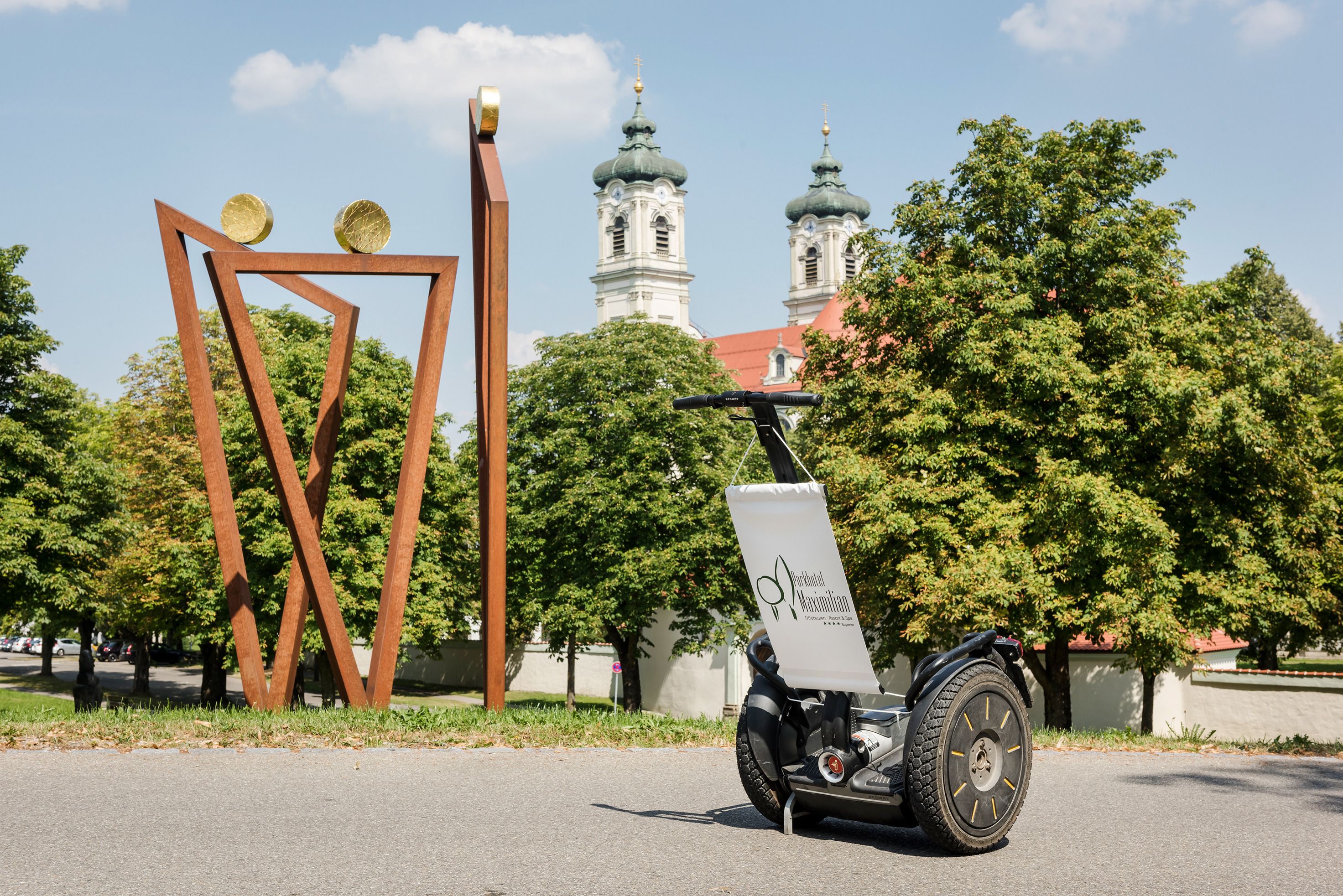 A Segway with a white sign in a park with trees and a church in the background.