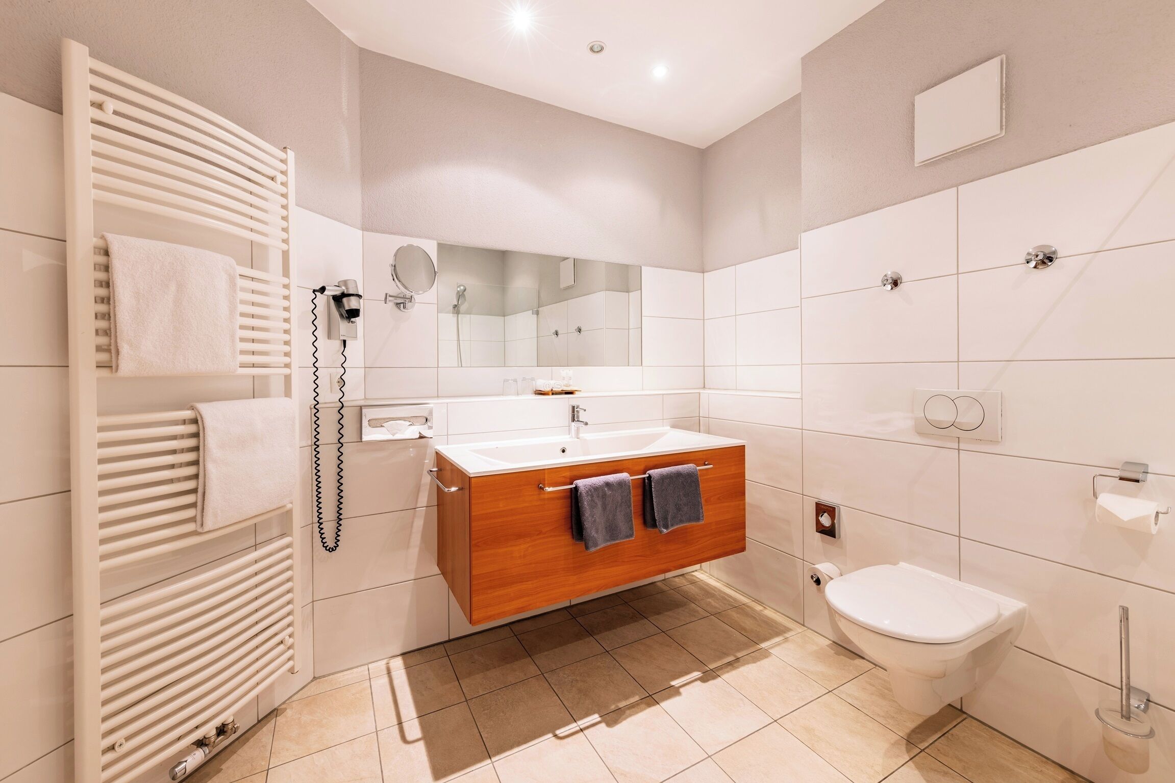 Ein modernes Badezimmer mit einem Holzbadschrank, einer weißen Toilette, einem Handtuchhalter und einem Spiegel.