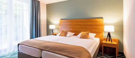 Una habitación de hotel con una cama grande, dos mesitas de noche con lámparas, un cabecero de madera y una alfombra estampada.