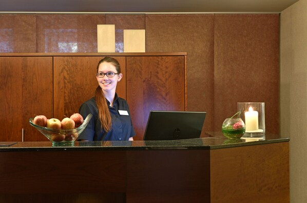 A reception desk with a laptop, a bowl of apples, and a candle.