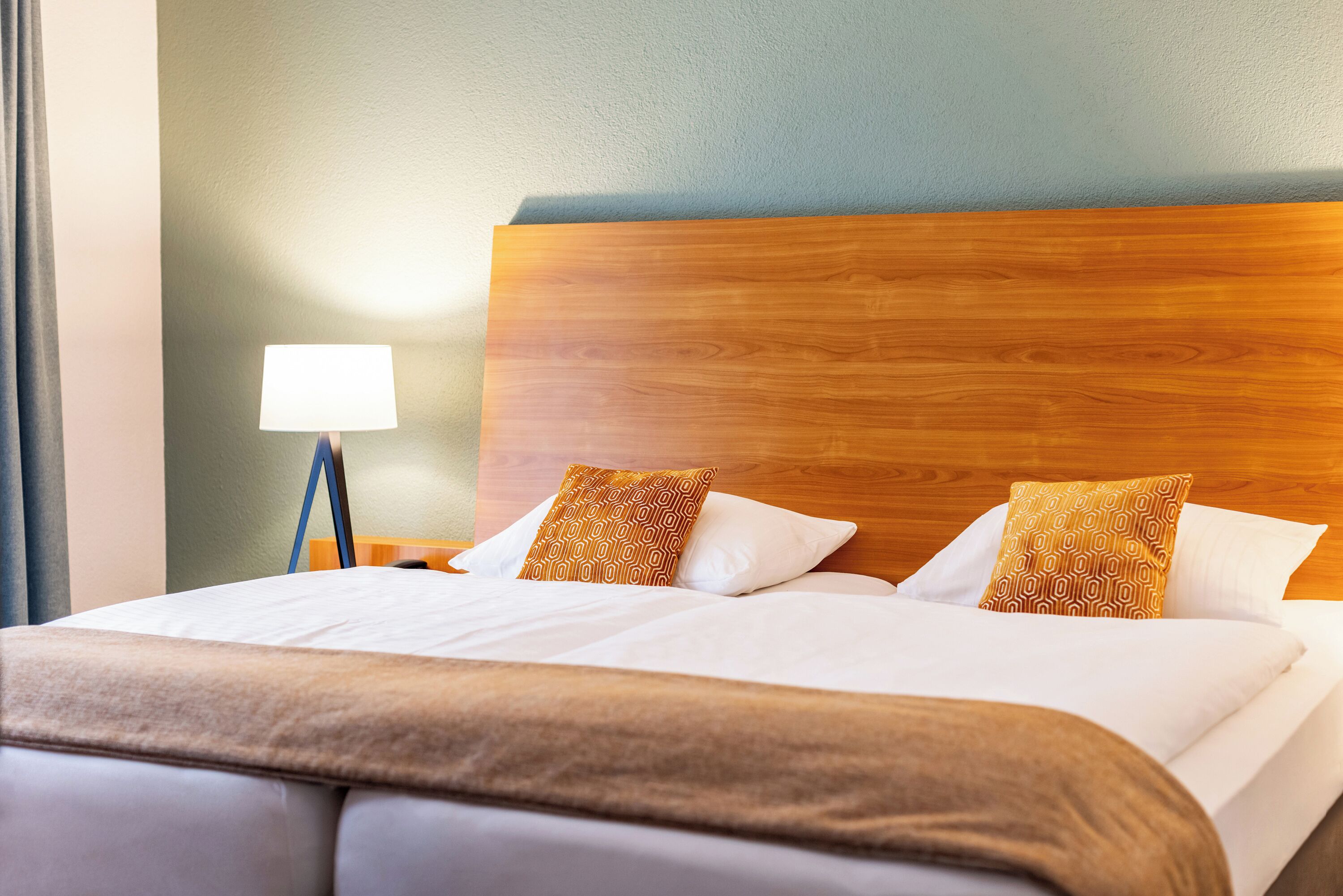 A hotel room with a wooden headboard, a bed with white linens, and a lamp on a nightstand.