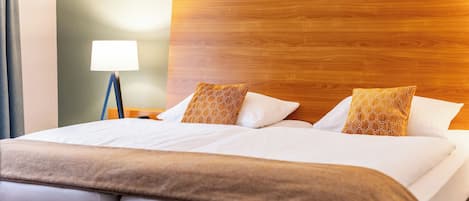 Una habitación de hotel con cabecera de madera, cama con ropa blanca y una lámpara en la mesita de noche.