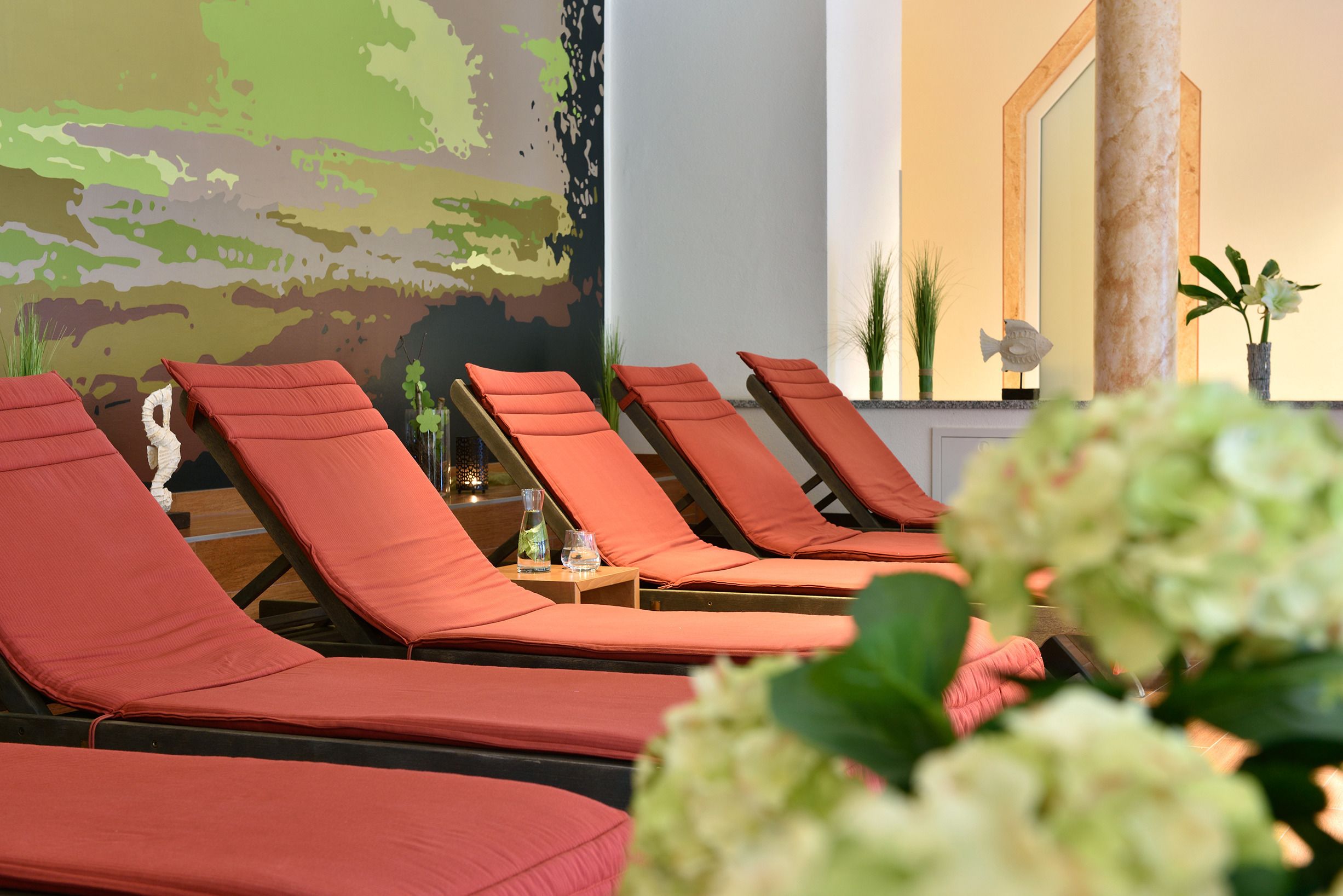 A row of sun loungers with orange cushions, a wall mural, and a mirror.
