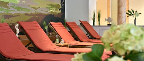 A row of sun loungers with orange cushions, a wall mural, and a mirror.