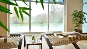 A room with two reclining chairs, a small table with a vase and glasses, and a large window overlooking a garden. - Parkhotel Maximilian Ottobeuren Resort&Spa (Ottobeuren)