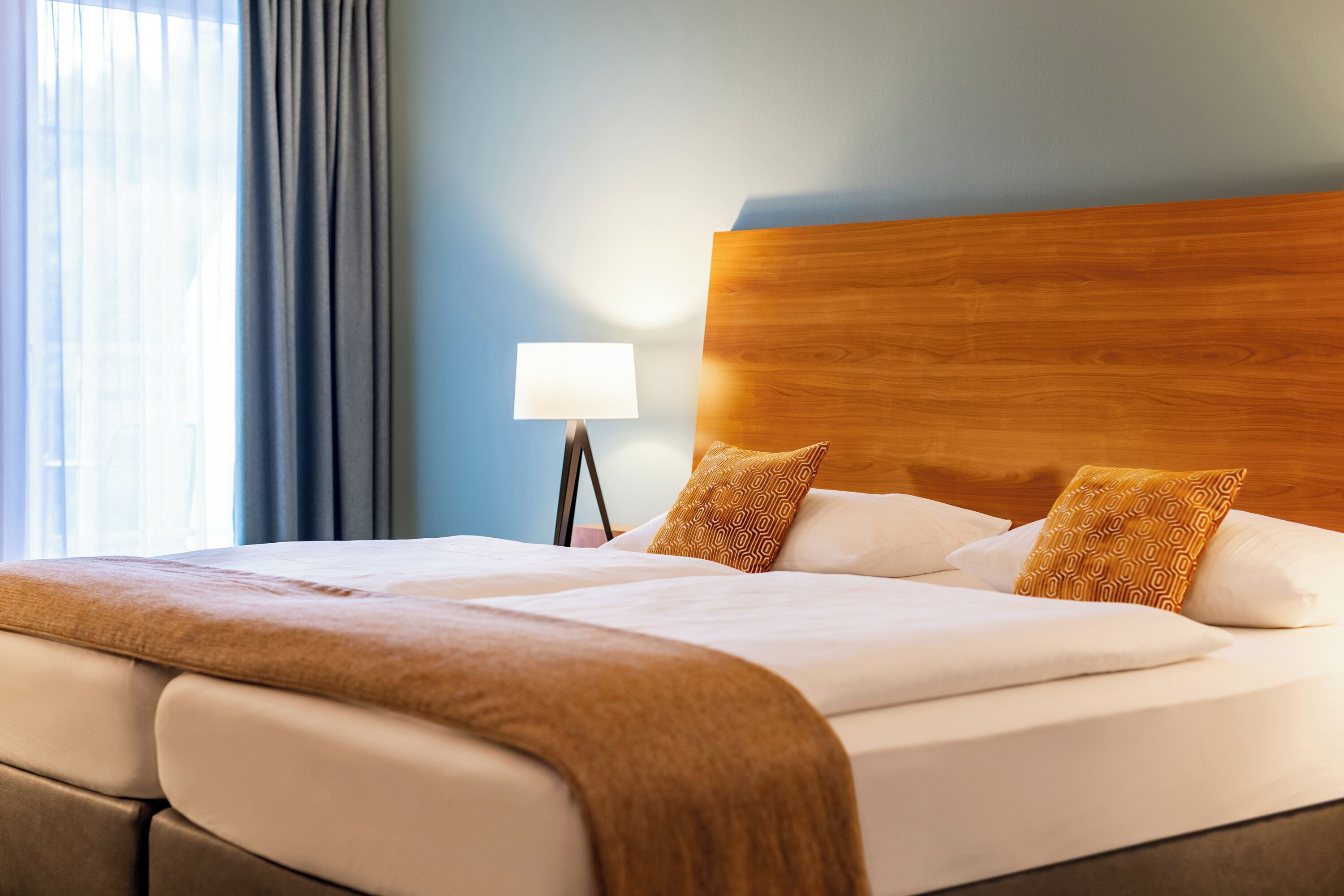 A hotel room with a large bed, two pillows, a bedside lamp, and a window with curtains.