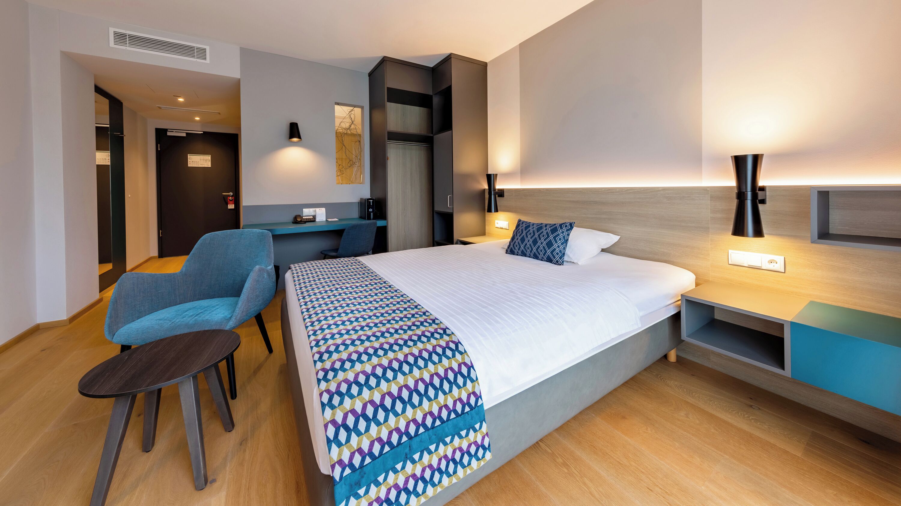 Une chambre d’hôtel moderne, dotée d’un grand lit, d’un bureau et d’une chaise.