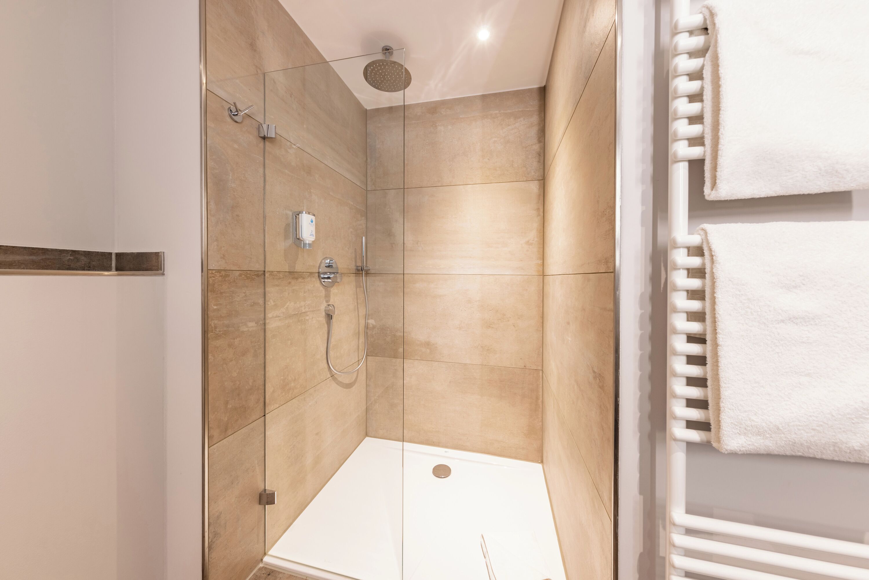A modern shower with a glass door, a wall-mounted towel rack, and a visible shower control panel.