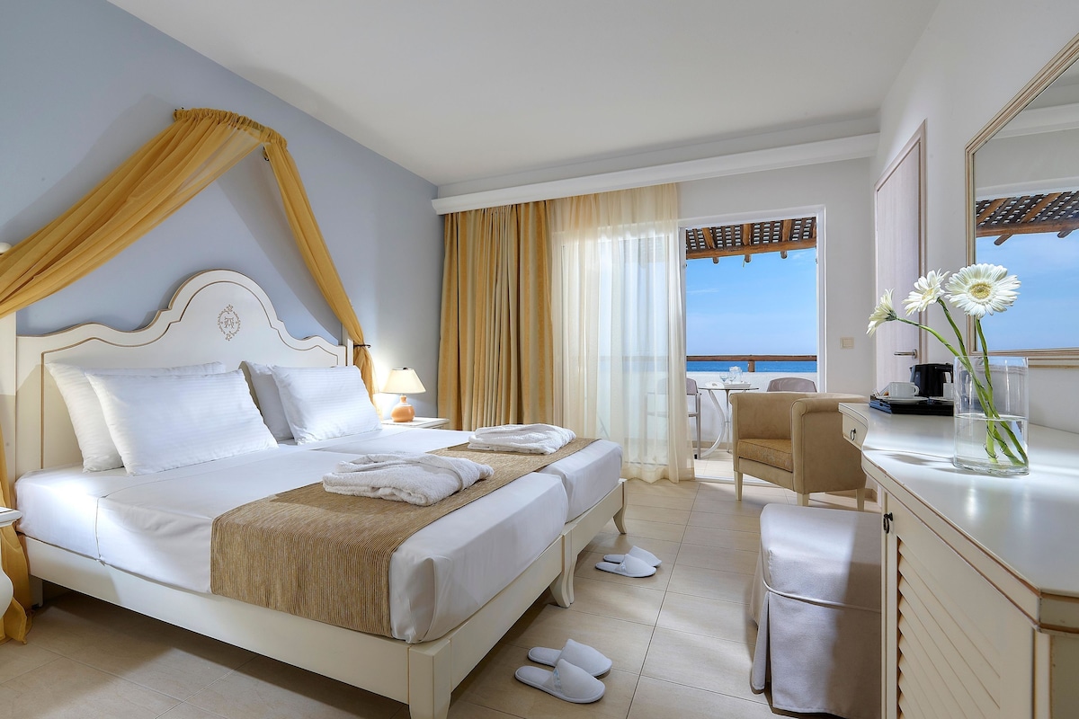 Ein Hotelzimmer mit einem großen Bett, einem Schreibtisch, einem Stuhl und Meerblick.