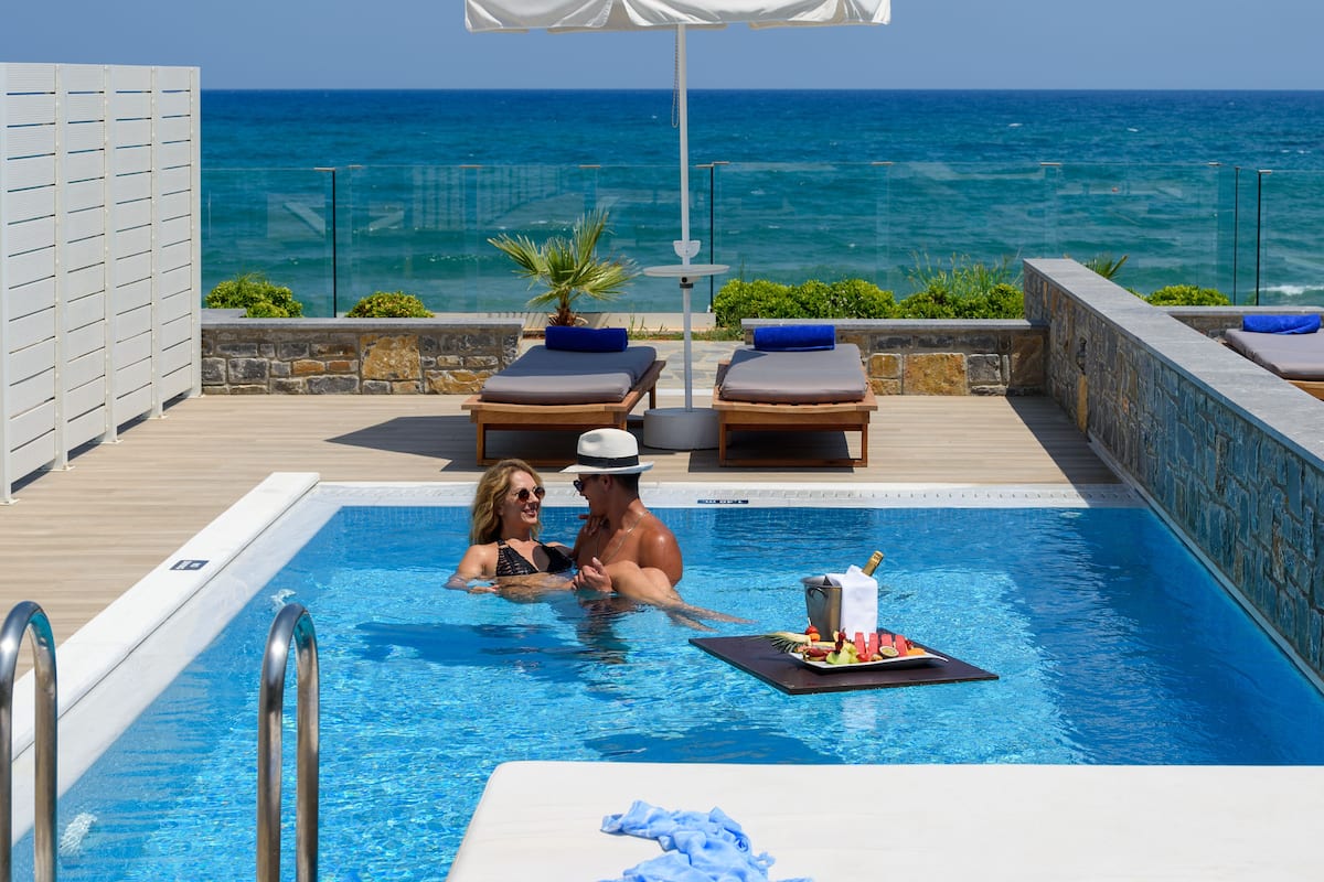 Zona junto a la piscina con vistas al océano, sillones de descanso y una mesa con bebidas y aperitivos.