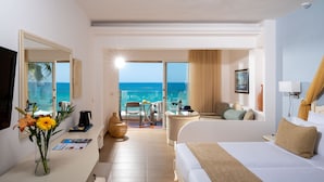 Une chambre d’hôtel comprenant un lit, un bureau avec une machine à café, une chaise, une table avec des boissons, une grande fenêtre donnant sur l’océan et un balcon avec vue sur l’océan.