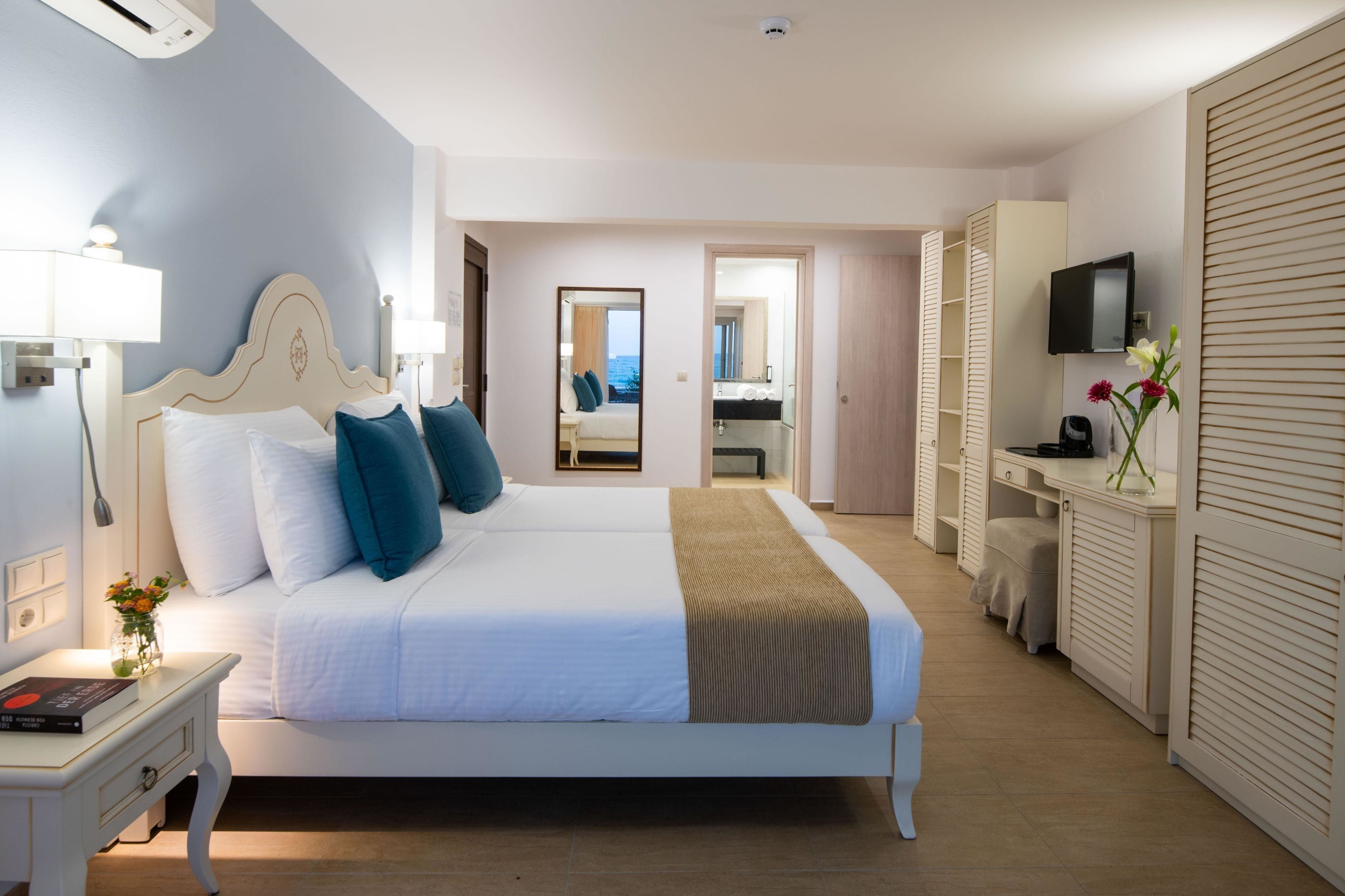 A hotel room with a large bed, bedside tables, a TV, and a bathroom visible through an open door.
