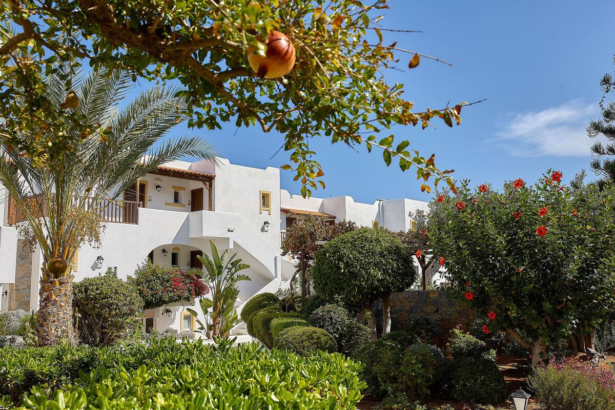 Un edificio blanco de fachada de piedra, rodeado de jardines cuidados y palmeras.