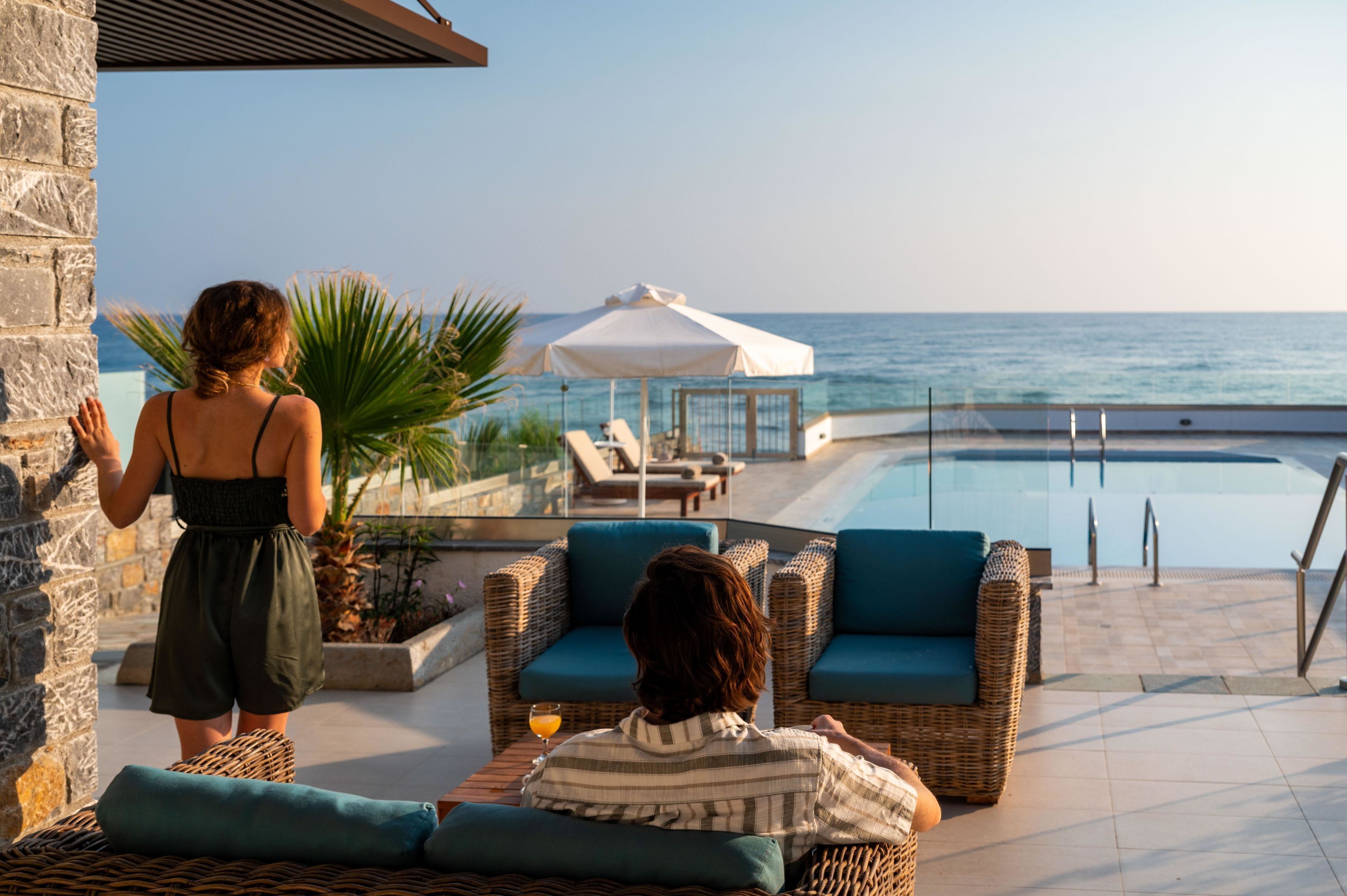 A poolside area with wicker furniture, a glass balustrade, and a view of the sea.