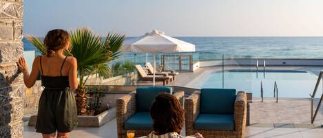 A poolside area with wicker furniture, a glass balustrade, and a view of the sea.