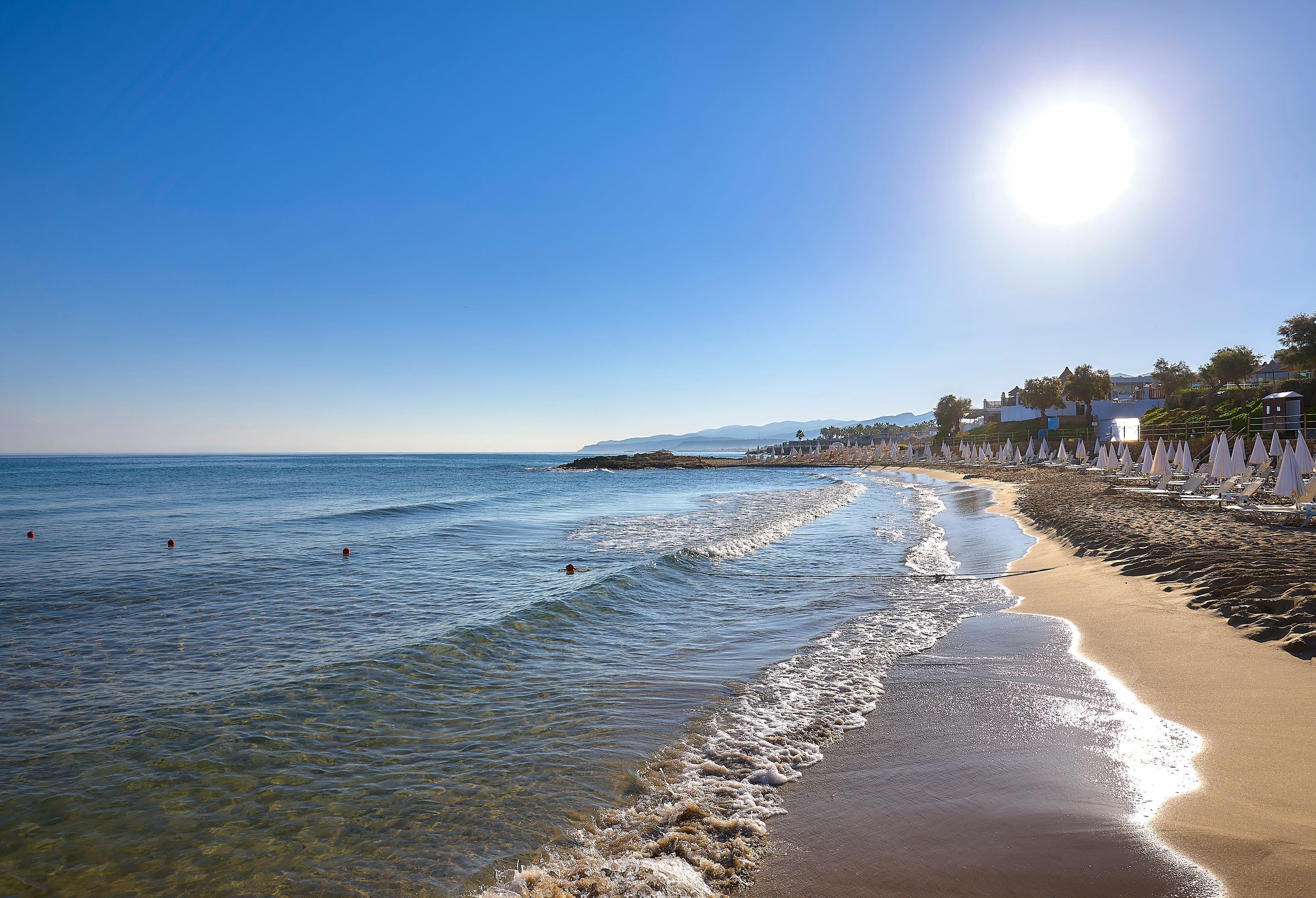 Una spiaggia con acqua cristallina, una riva sabbiosa e una fila di ombrelloni bianchi.