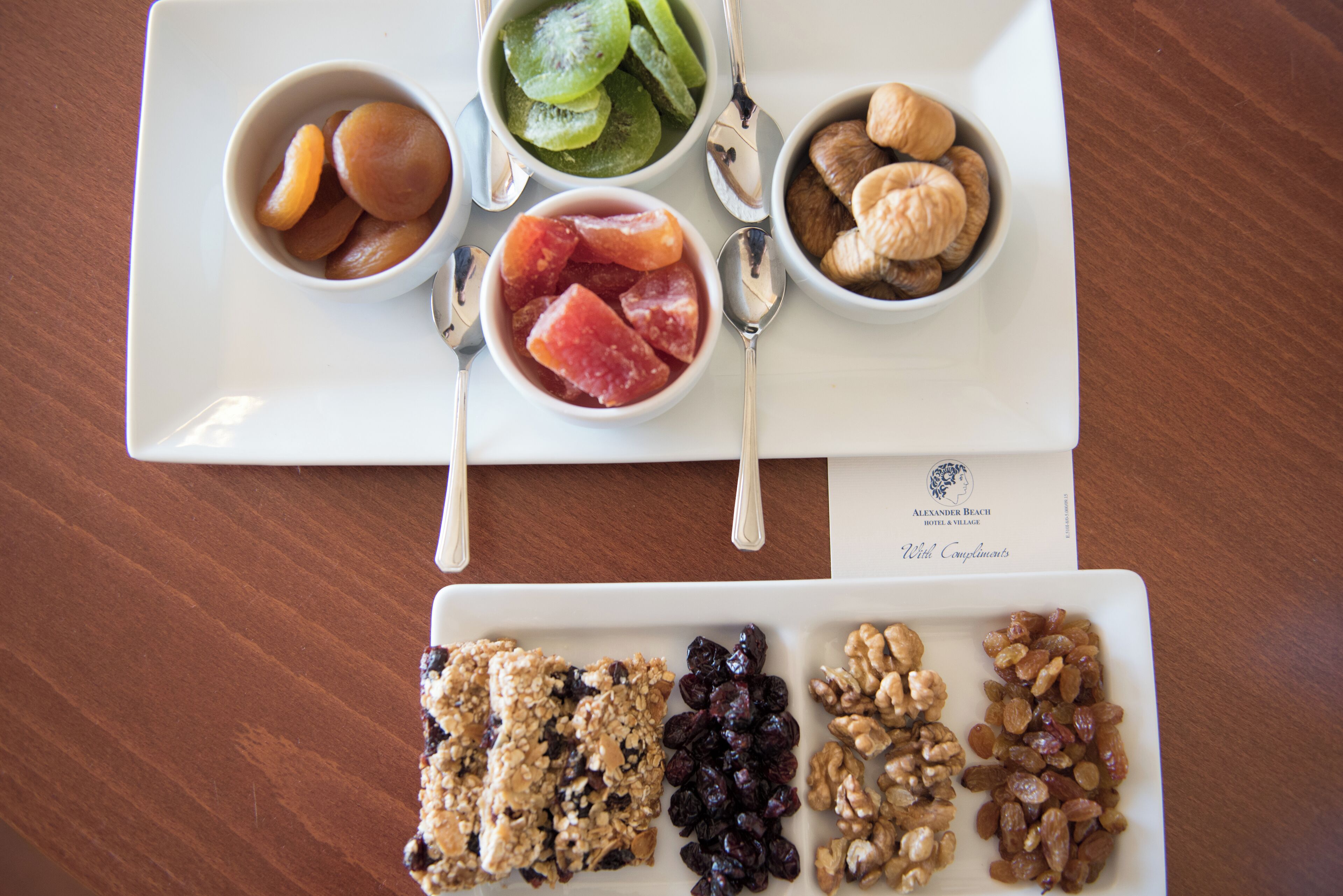 Bandeja blanca con diversos alimentos, entre ellos frutas, nueces y barras de granola.