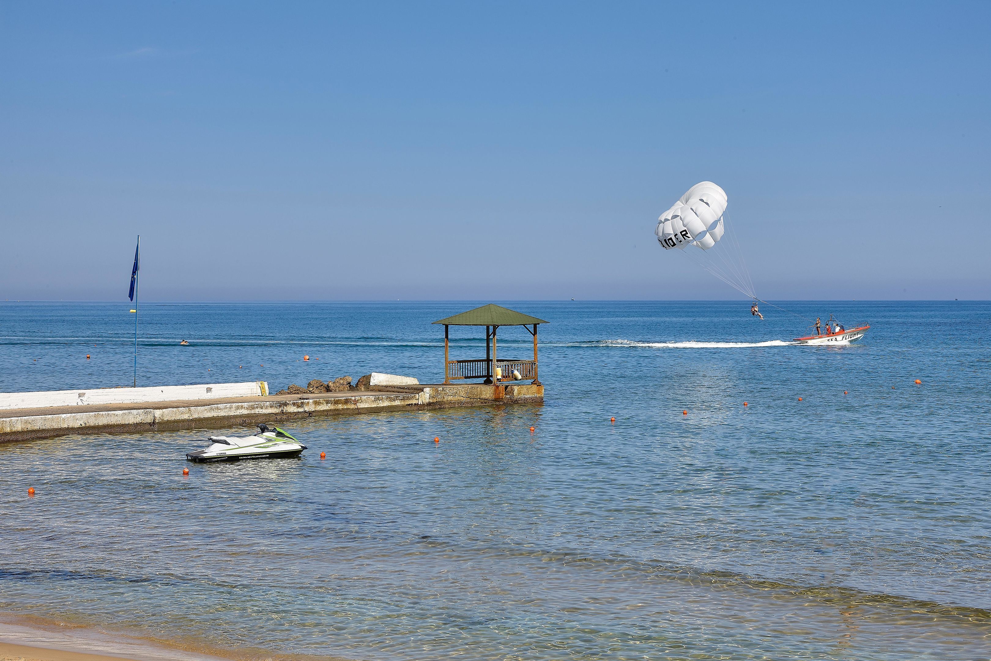 Ein Strand mit Jetski, Fallschirm und einem kleinen Boot.