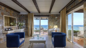 Une pièce avec un mur en pierre, un plafond en bois et une grande porte-fenêtre coulissante donnant sur un balcon avec vue sur la mer.