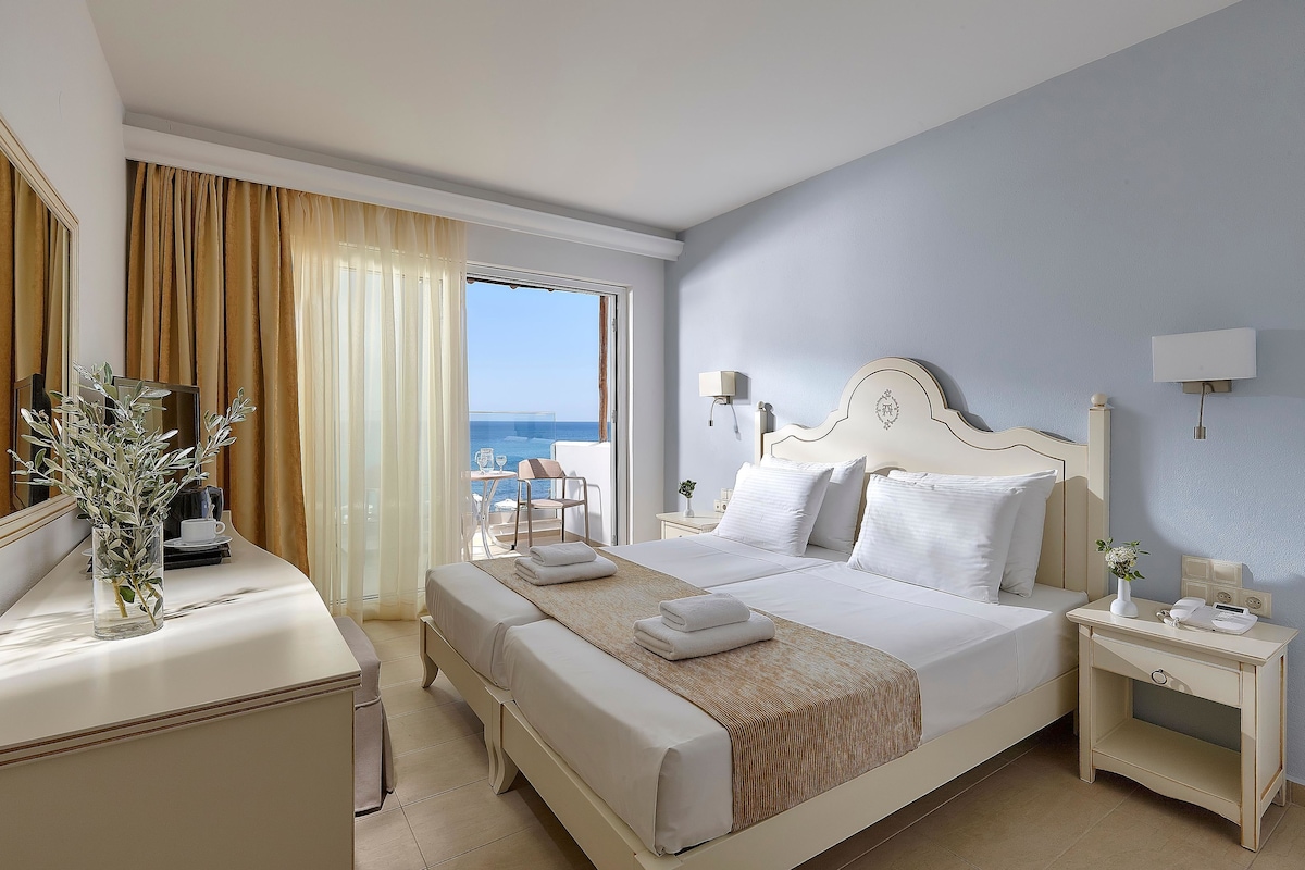 Ein Hotelzimmer mit Bett, Nachttischen, einem Schreibtisch mit einer Vase und Meerblick.