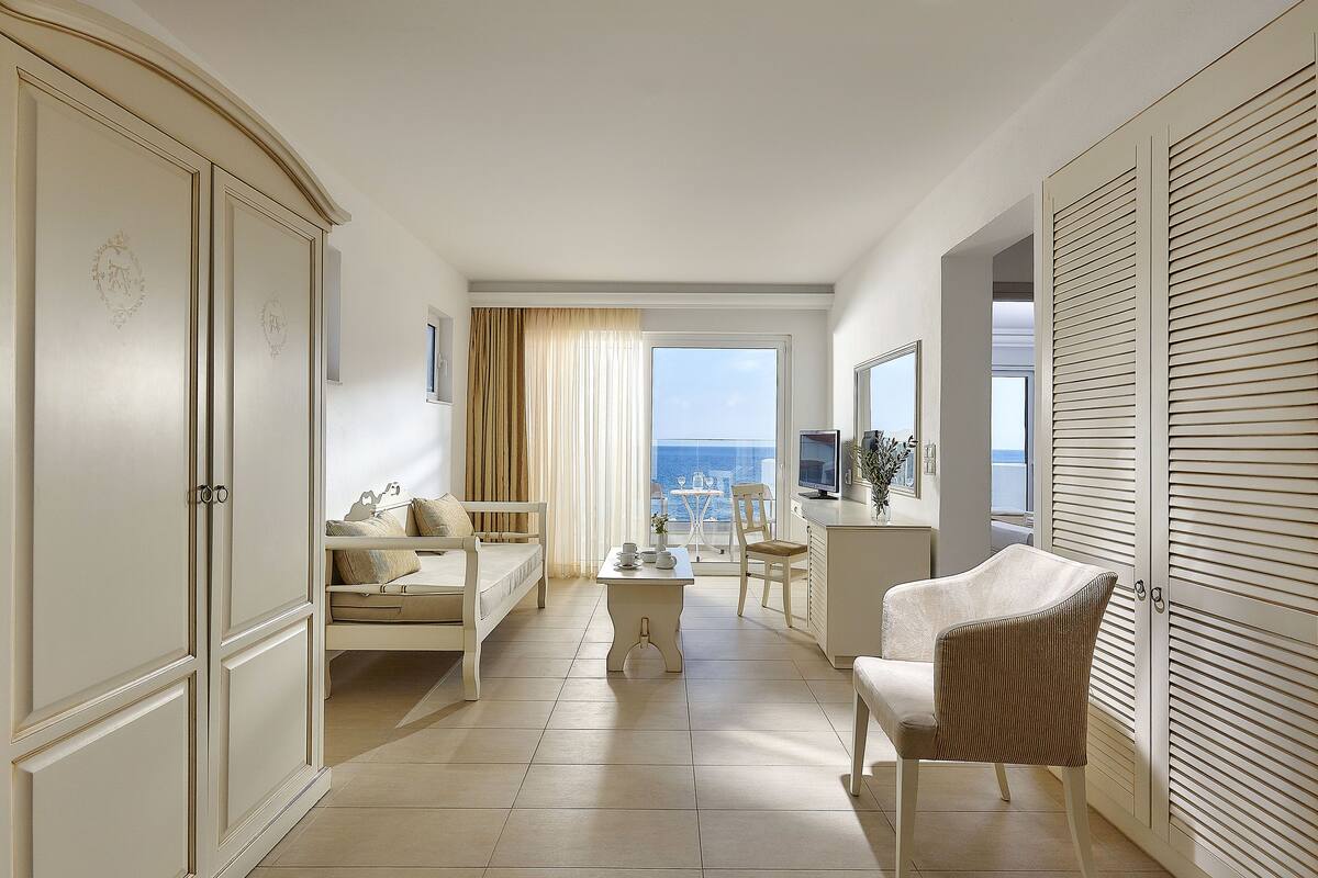 Una habitación de hotel con balcón, un sofá, una mesa de comedor y una silla.