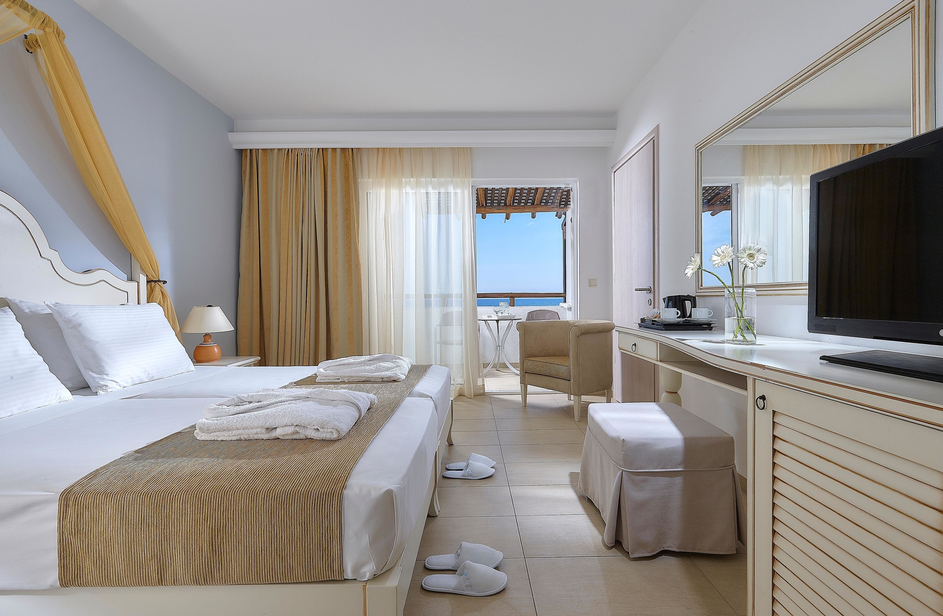 Ein Hotelzimmer mit Bett, Schreibtisch, Stuhl, Fernseher und Meerblick.