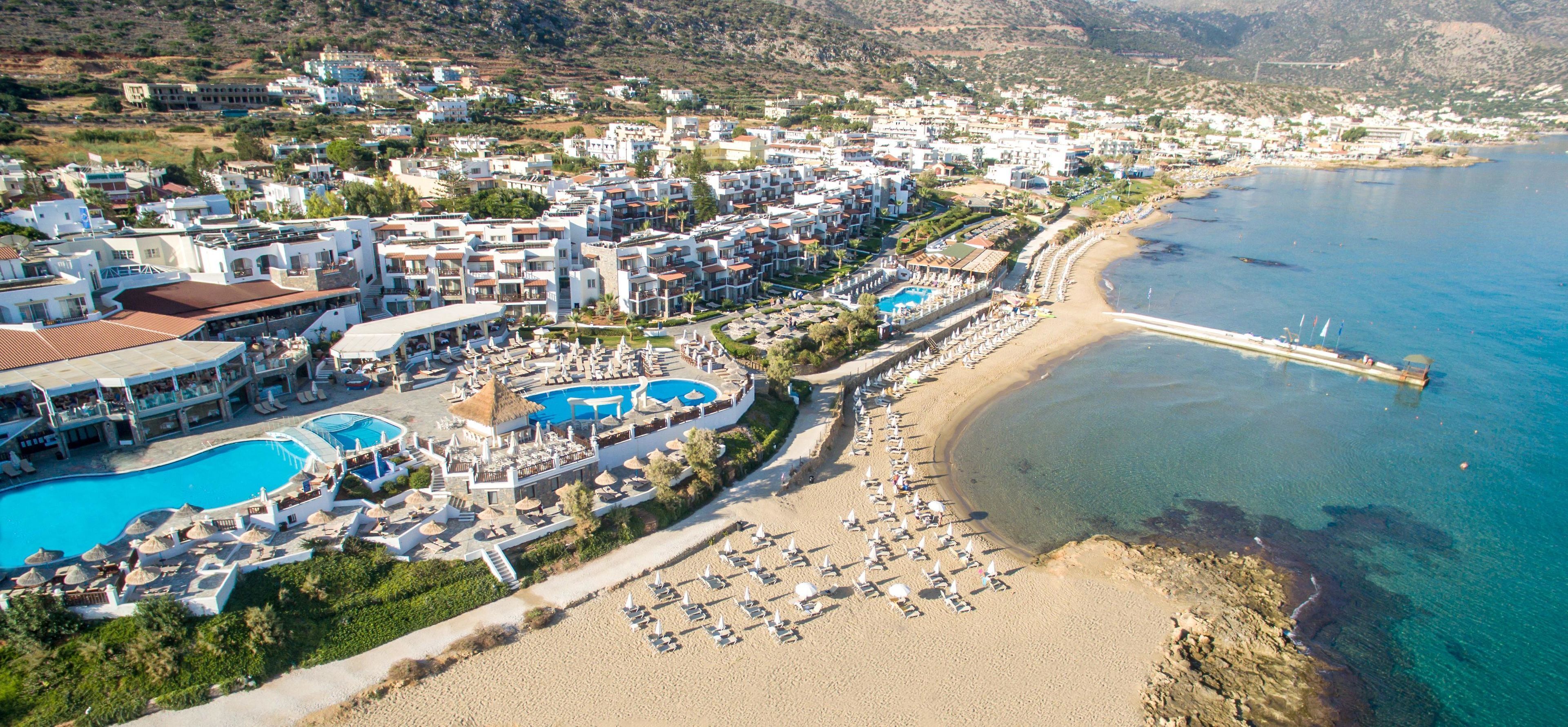 An aerial view of a coastal resort with multiple swimming pools, beachside lounge areas, and a pier extending into the sea.