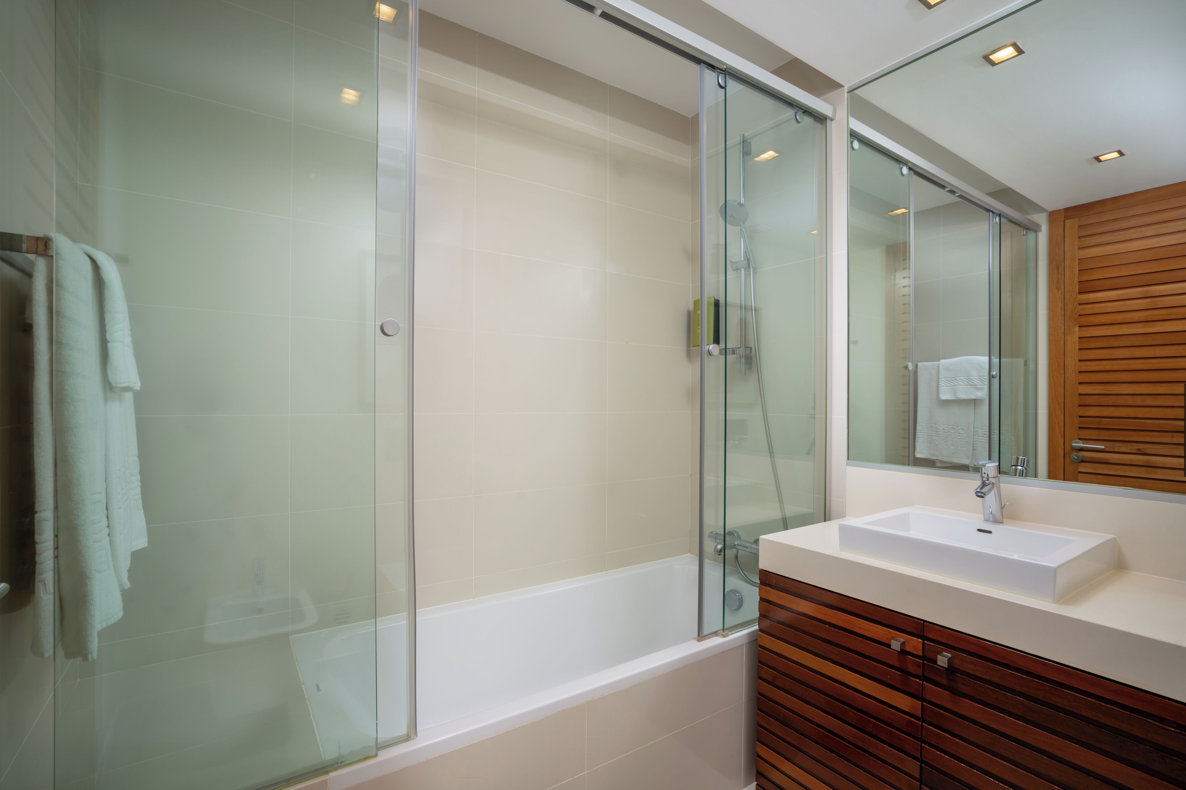 Een moderne badkamer met een douchecabine van glas, een witte wastafel en houten opbergkasten.