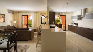 Une cuisine moderne dotée d’un îlot central, d’un coin repas avec un canapé et des chaises, et offrant une vue sur l’extérieur grâce à de grandes fenêtres.
