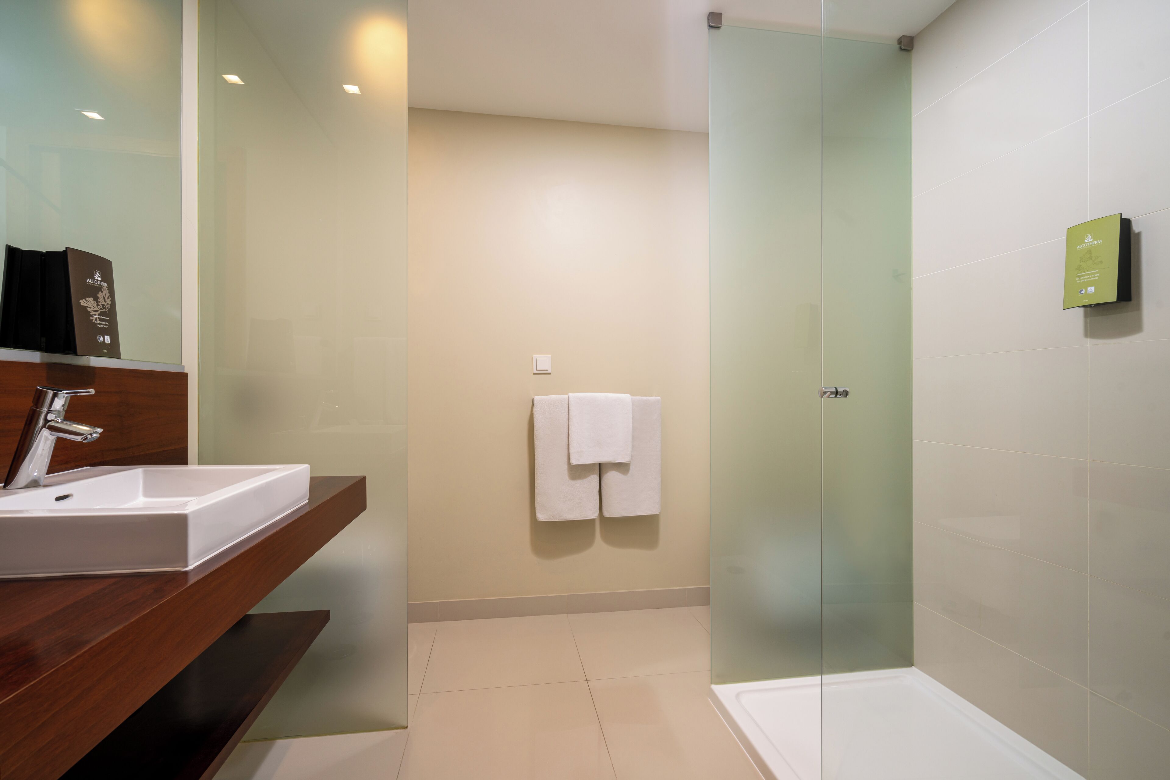 A modern bathroom with a white sink, a glass-enclosed shower, and a green information panel.